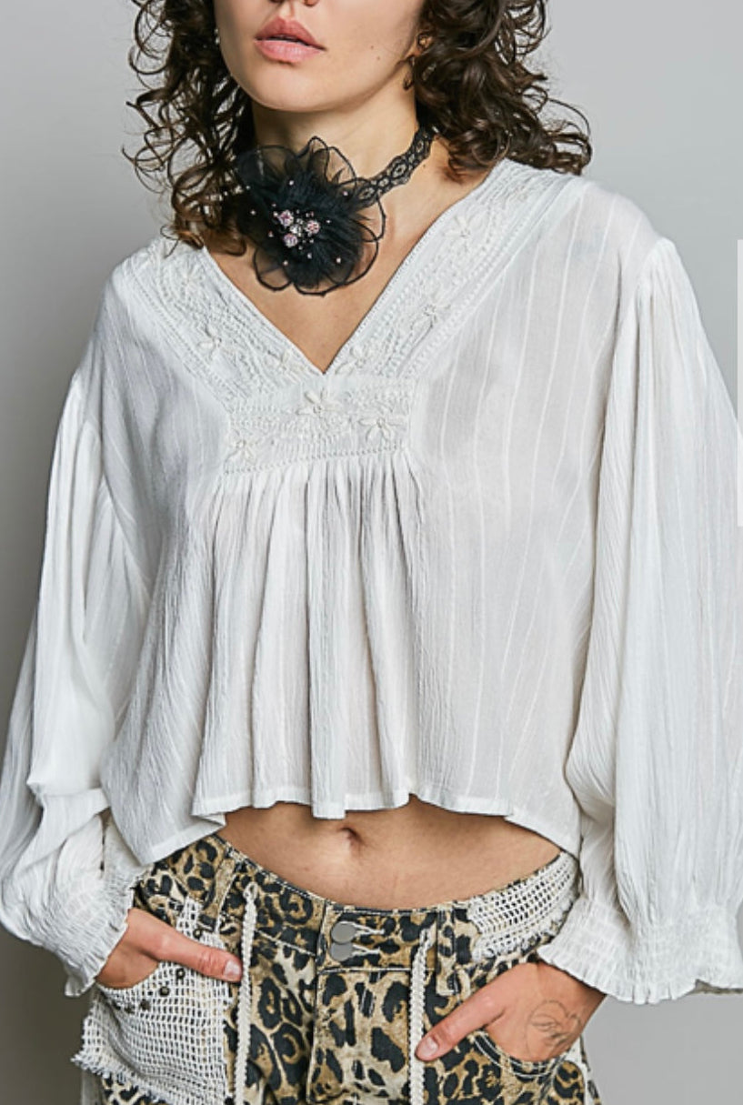 A woman wearing a loose white long-sleeve blouse with a gathered peplum-style hem and patterned leopard-print pants, posed against a light gray studio background.