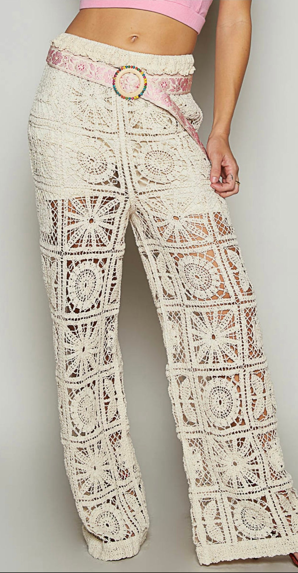 A pair of white lace crochet pants with a belt, displayed on a model