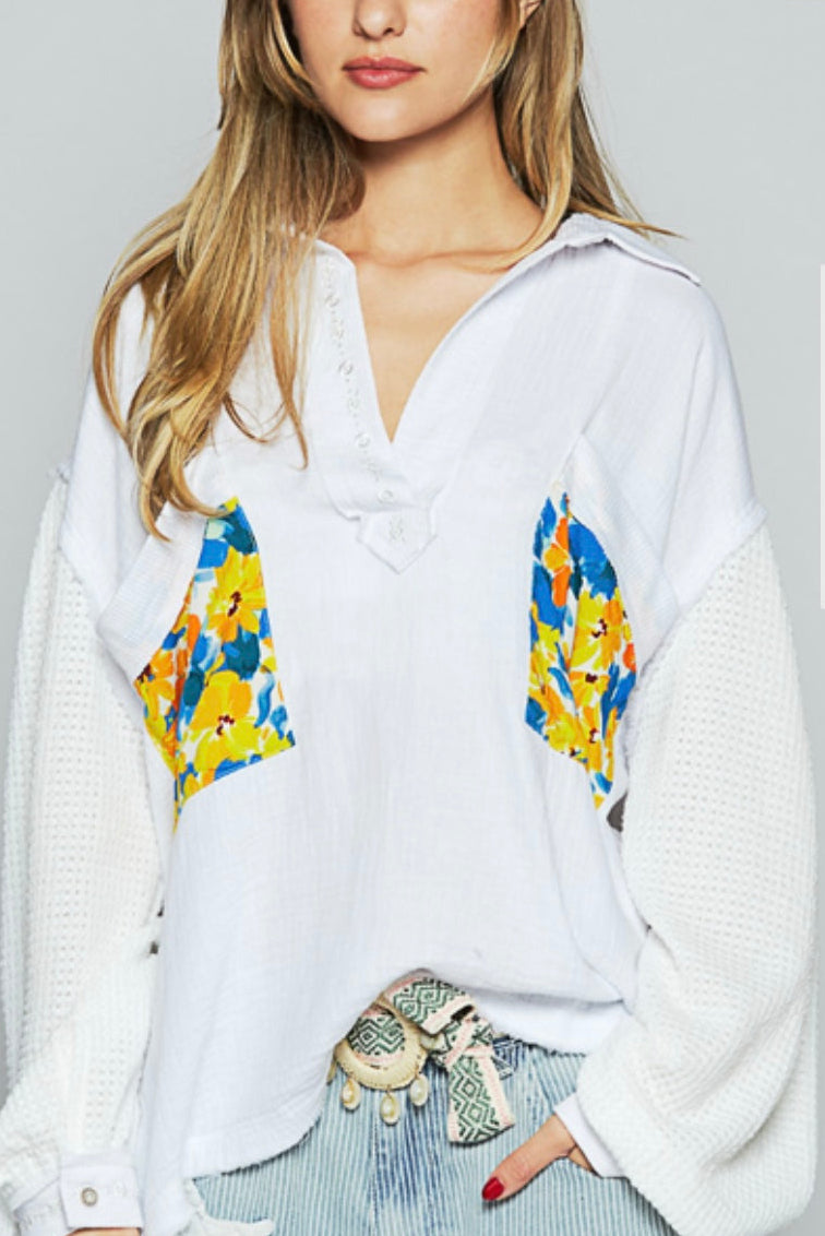 A woman wearing a white oversized cotton gauze top with accent pockets featuring a floral pattern in multicolor, paired with blue denim pants.