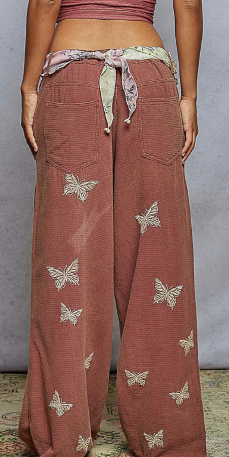 rust wide-leg pants with butterfly patterns worn by a person, on a neutral background.