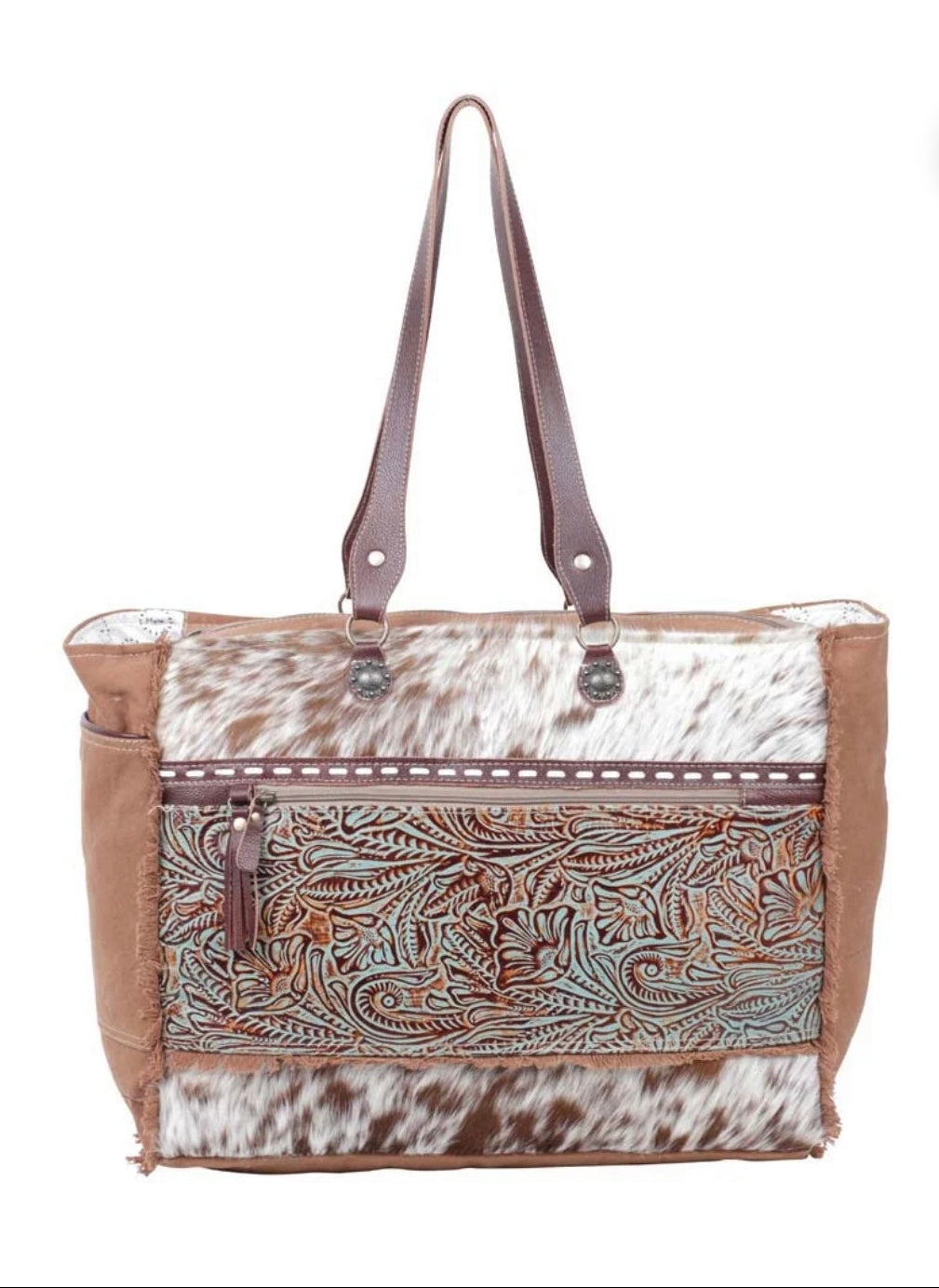 A western-style tote bag featuring brown leather handles, a brown faux-suede side panel, and a front panel combining brown and white cowhide with an embossed floral pattern.