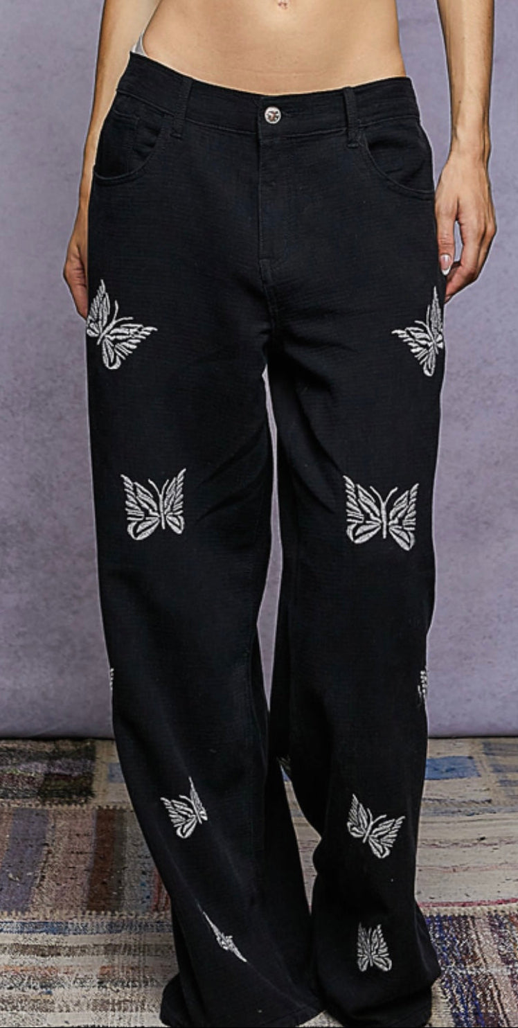 Black pants with butterfly patterns worn by a person against a gray background