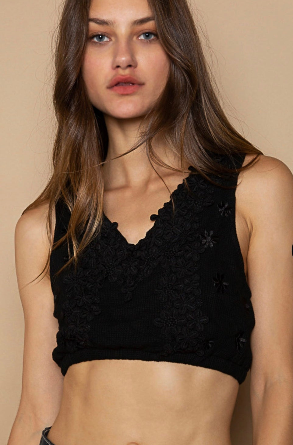 A woman wearing a black floral embellished knit V-neck crop top and blue denim shorts.