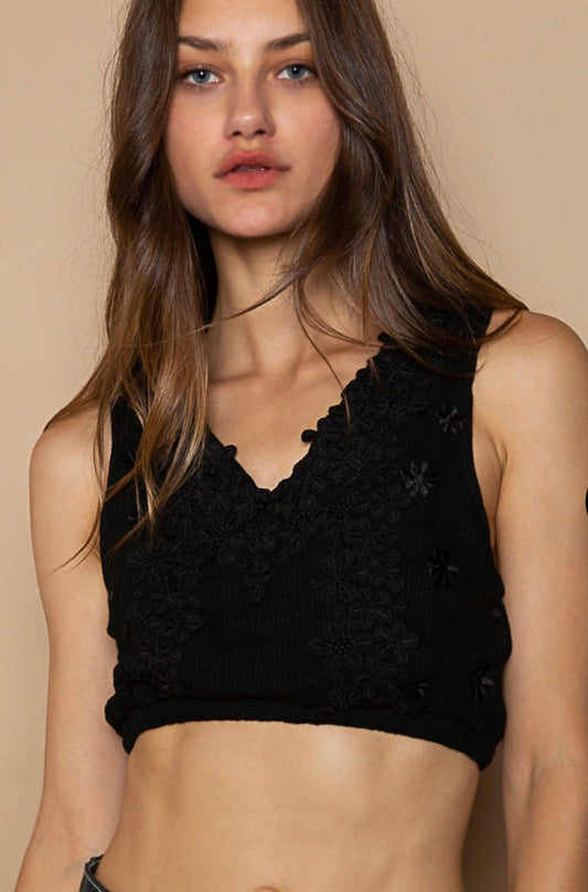 A woman wearing a black floral embellished knit V-neck crop top and blue denim shorts.
