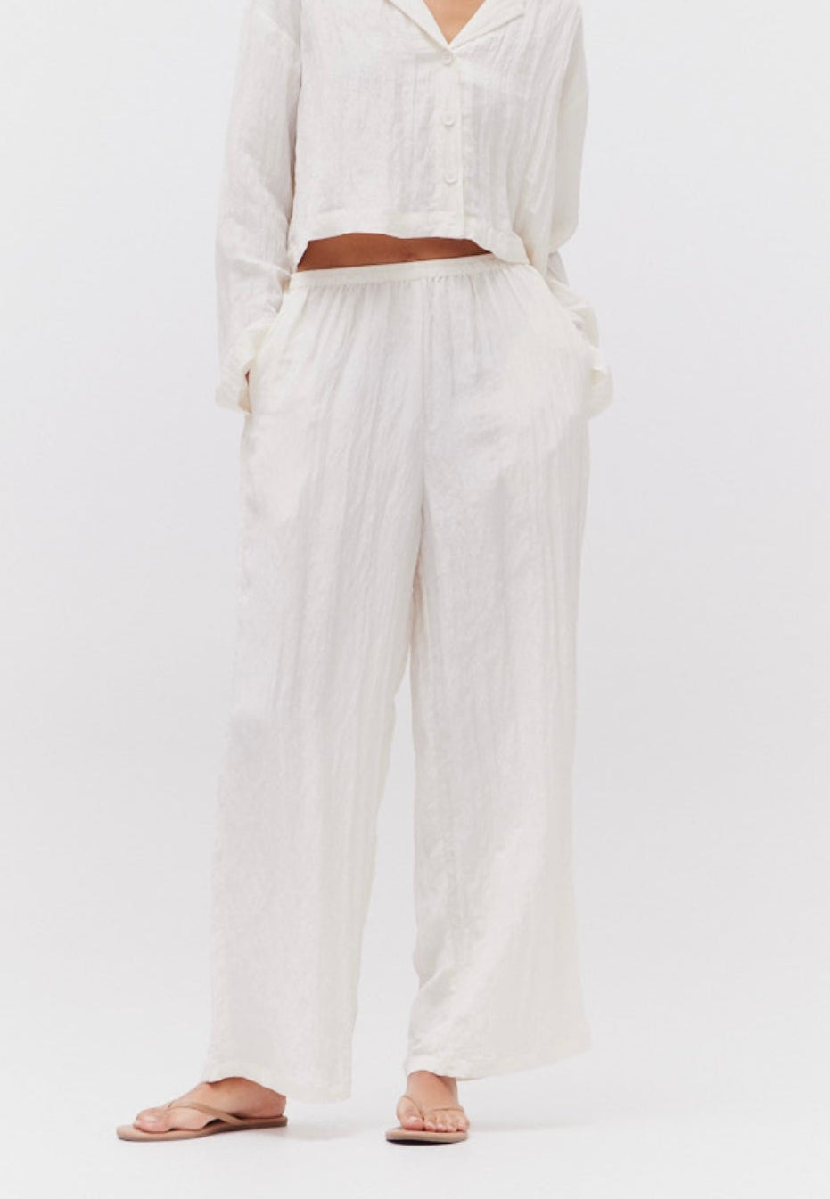 A person wearing white crinkle pants with pockets and an elastic waist.